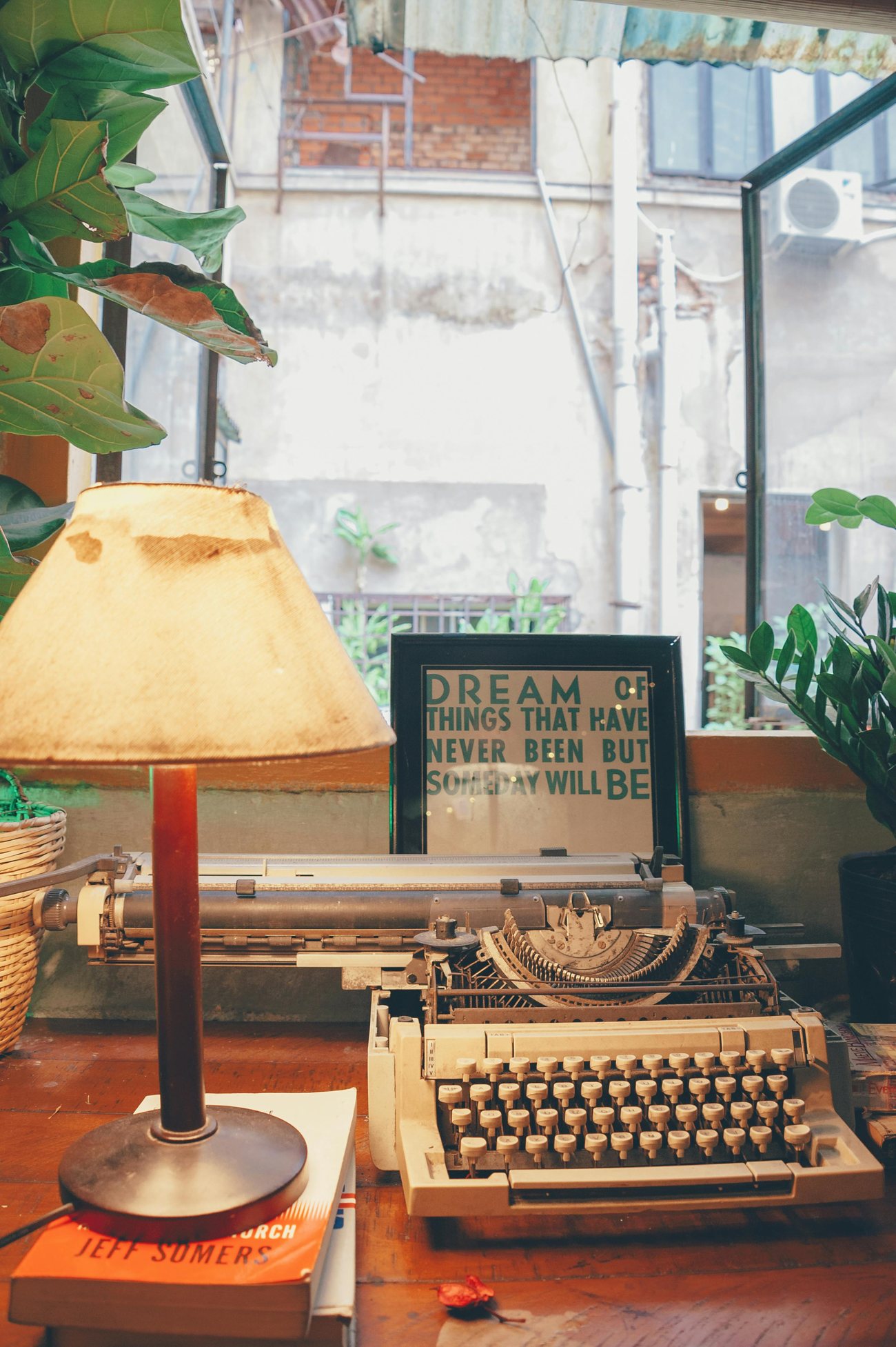 A vintage typewriter and lamp on a wooden desk by a window