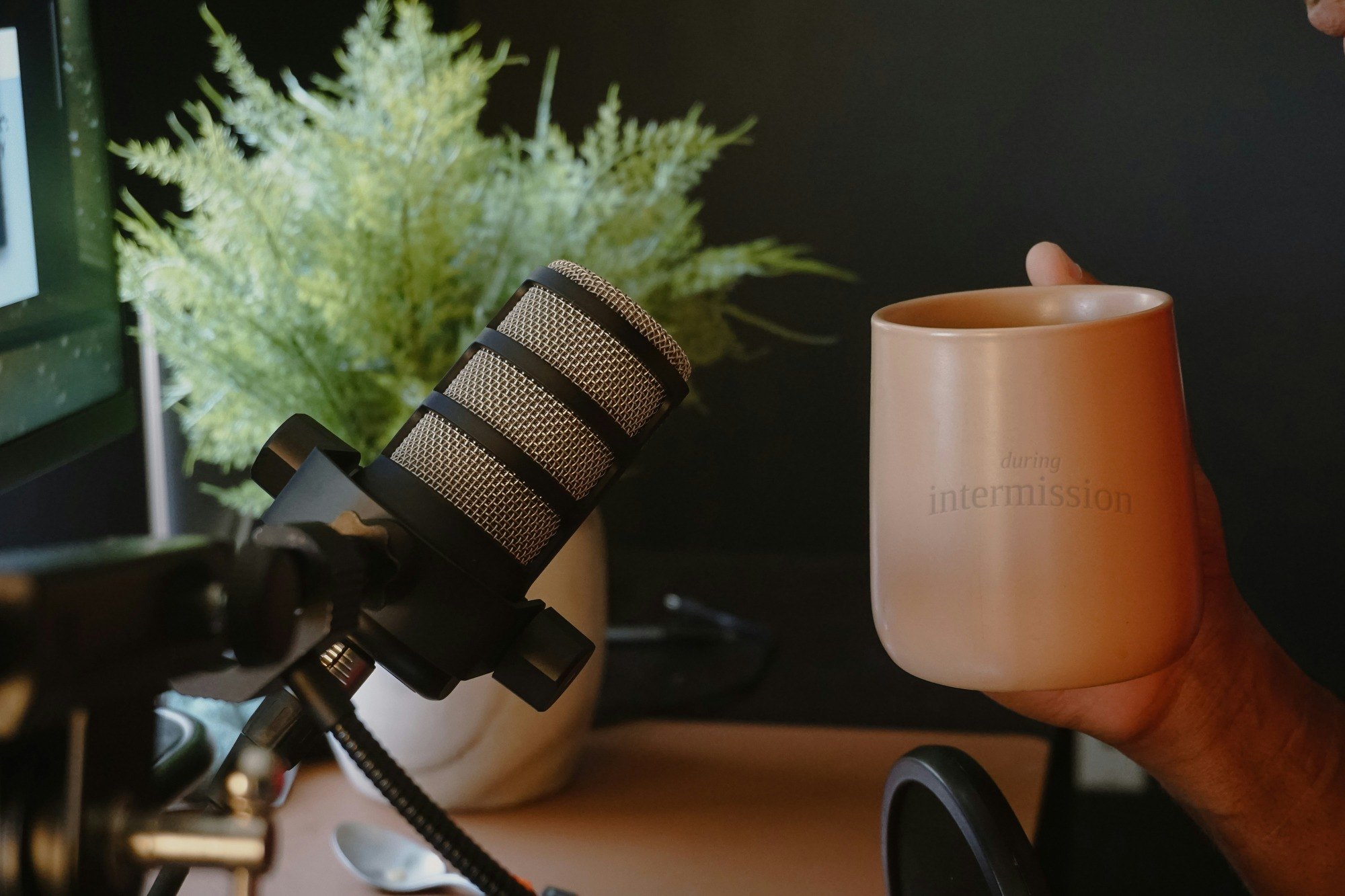 A quiet podcast desk with a microphone, a plant, and a warm mug engraved during intermission